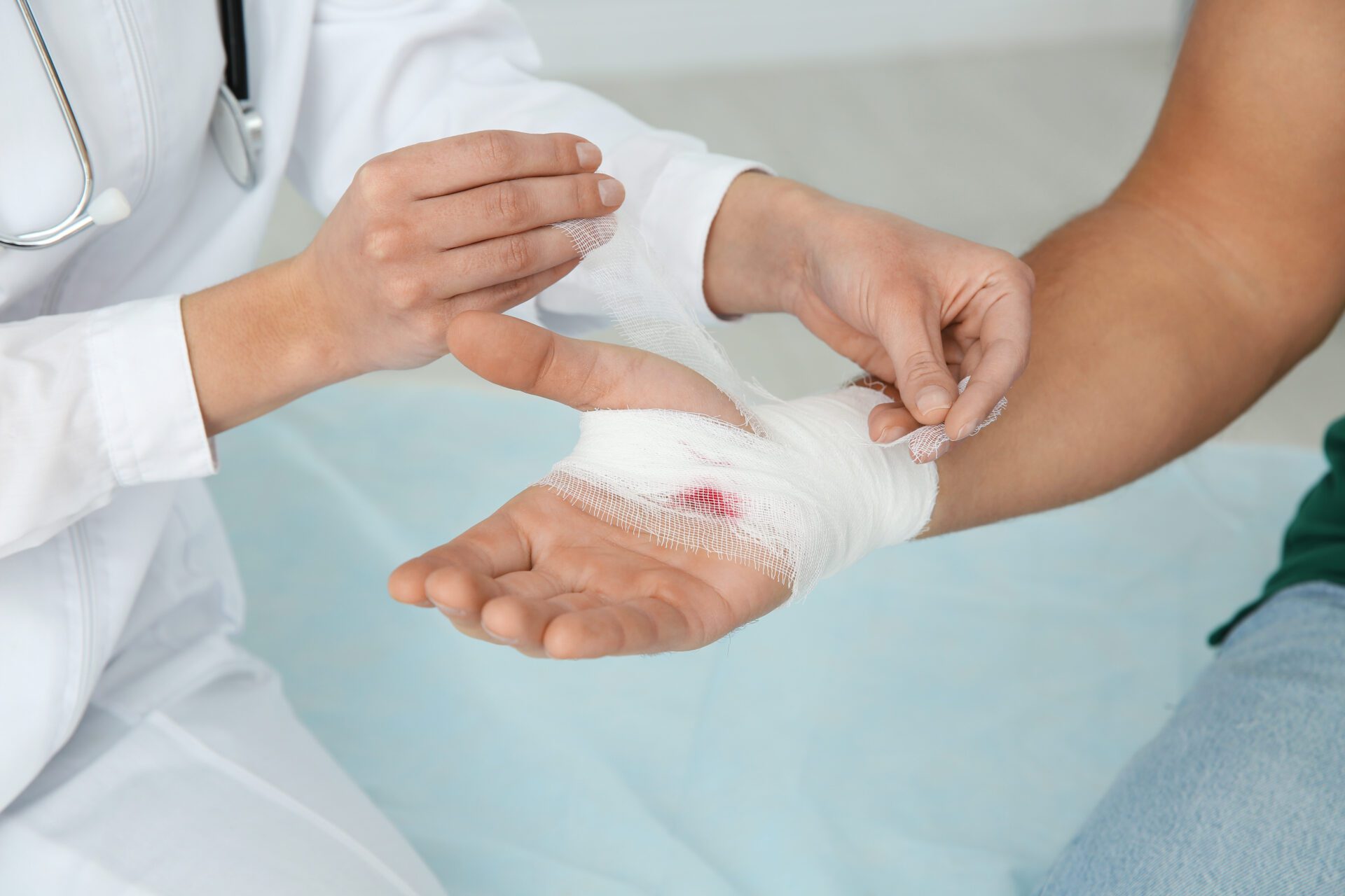 Female doctor applying bandage on young man's hand in clinic, closeup. First aid Female doctor applying bandage on young man's hand in clinic, closeup. First aid